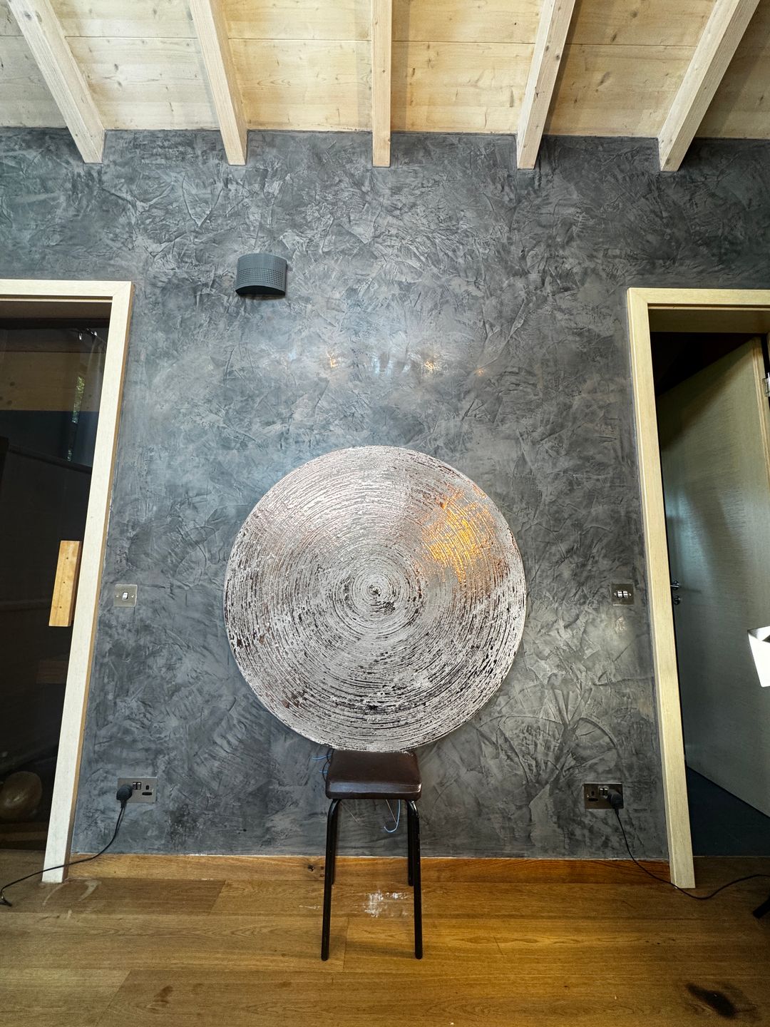 Silver circular panel on a charcoal plaster wall beneath timber beams